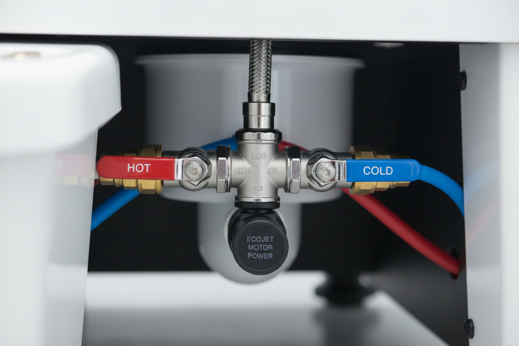 Close-up of plumbing manifold connection at chair base showing shared supply line fitting, hot/cold valves, and ECOJET motor power connector
