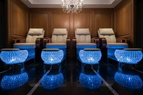 Four MYSTIQUE pedicure chairs in a row with all four crystal bowls illuminated in deep blue, chrome bases reflecting, low angle on polished dark floor