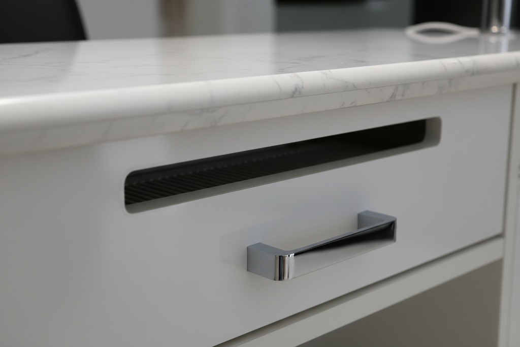 Close-up of PRIVÉ nail table integrated ventilation slot opening, gel-coated marble edge profile, and chrome drawer pull hardware detail